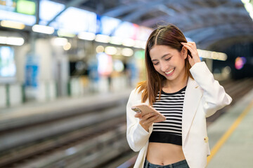 Young asian woman using smartphone application navigate location destination while travel by train. Asian female with cell phone standing near railway platform in train station.