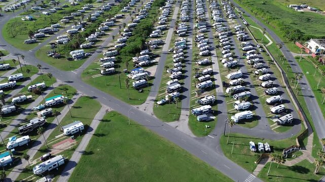 Entrance to large premium RV sites with concrete pads, full hook-ups, picnic tables, fire rings, resort amenities in South Padre Island beach, long row of recreational vehicles trailers boats, TX