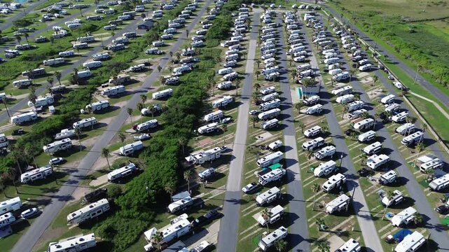 Long row of RV campers with travel trailers, cars, boats in premium RV sites with concrete pads, full hook-ups, picnic table in South Padre Island beach, Texas, flyover recreational vehicles park