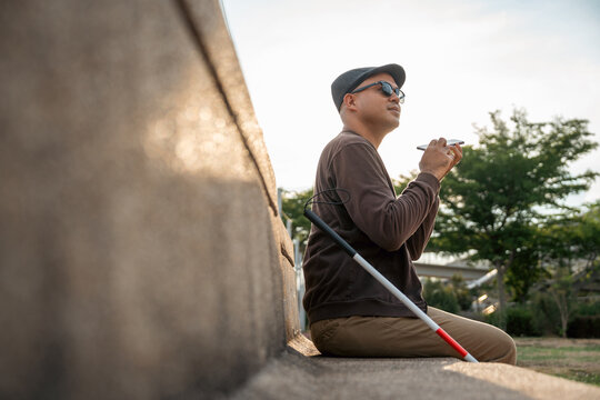 Young asian blind man using application on mobile phone to helping accessibility for persons with visual impairment. Technology for blind people sending voice message or navigation.
