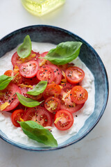 Bowl of fresh stracciatella cheese served with sliced tomatoes and basil, vertical shot, selective focus, middle close-up