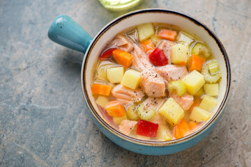 Vegetable soup with salmon in a turquoise serving bowl, horizontal shot on a grey and beige granite background, elevated view
