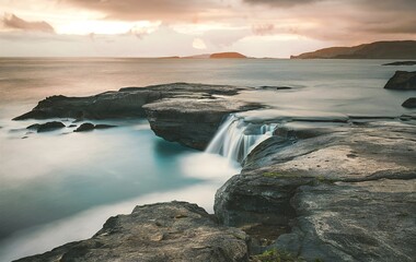 A series of rock formations jut out into the sea, with one of them having a small waterfall cascading over its