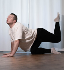 Fototapeta premium Home yoga pose workouts. A man performs sports exercises with his legs and arms. Male athlete stretches.