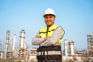 Asian engineer man with safety helmet standing front of oil refinery. Industry zone gas petrochemical. Factory oil storage tank and pipeline. Workers work in the refinery construction building