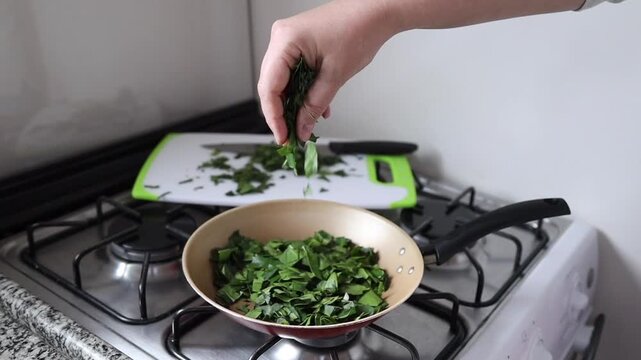 Hands cooking ora-pro-nobis (Pereskia aculeata) in a frying pan, a popular edible plant in Brazil