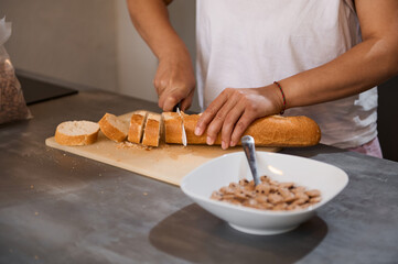 Person slicing bread for breakfast in a modern kitchen with a bowl of cereal on the counter