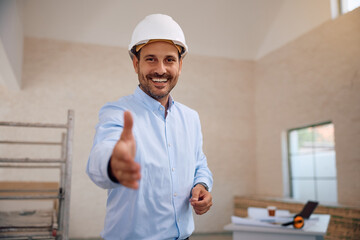 Happy architect offering  handshake at construction site and looking at camera.