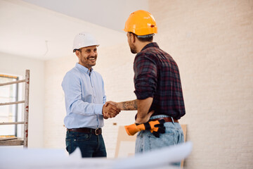 Happy building contractor shaking hands with aworker at construction site.