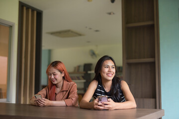 Two Beautiful Asian Woman Sitting Indoors in Coworking Space Style Library Office Using Smart Phone