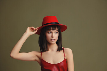 Fototapeta premium Young woman in a red hat and leather dress posing against a green background