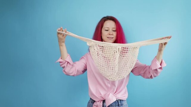 Net bag, Woman with pink hair with reusable mesh on blue background , carrying cotton textiles for environmental awareness