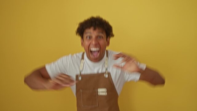 Cheerful hispanic man celebrating in a brown apron against a vibrant yellow background.
