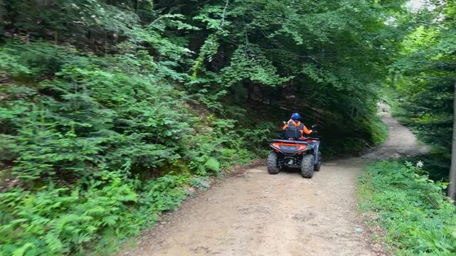 Mountains road with quad bikes on driving down the path in summer forest. ATVs vechicle on journey to the mountains.People, leisure and vacation concept.