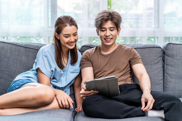 Obraz premium Portrait of an happy couple in love using a tablet, looking at digital computer tablet screen, relaxing on comfortable couch. Loving couple shopping online in internet store.