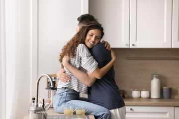 Pretty enamored woman sitting on kitchen countertop and cuddling beloved man, hugging husband, enjoy moment of tenderness, feeling love, express caress, giving support. Romantic dating, relationships