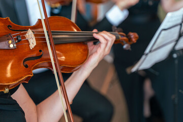 Close-up of a professional violinist of a symphony orchestra playing on the stage of a classical theater during a musical concert. Performers play music for the audience