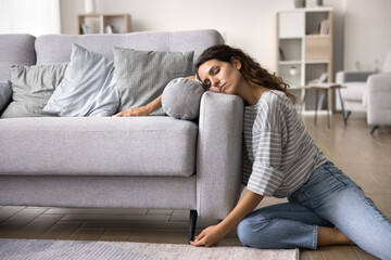 Young fatigued, overworked woman leaning against sofa, rests after hard work, fell asleep on floor...