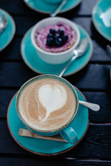 Coffee with milk in the shape of a heart with foam and blueberry cheesecake on a plate in cafe