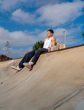 young man skater sitting on the edge of the bowl in a skate park