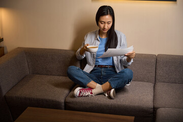 Fototapeta premium Focused woman looking through documents sitting on sofa