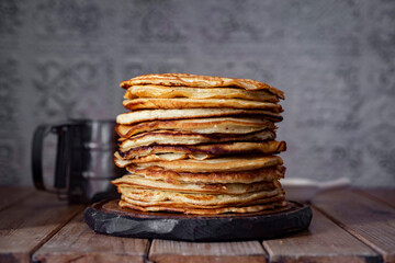 A stack of pancakes on a wooden table on a gray background. Thin pancakes for breakfast for the whole family. Close-up.