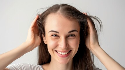 Fototapeta premium A young woman with long hair, smiling and touching her hair with both hands. The light and airy room enhances her cheerful and carefree demeanor, creating a sense of happiness and relaxation.