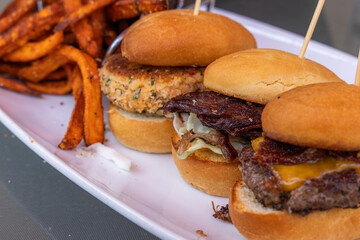 Three sliders with cheese and bacon, pulled pork and a crab cake served on buns, with a side of fries.