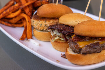 Three sliders with cheese and bacon, pulled pork and a crab cake served on buns, with a side of...