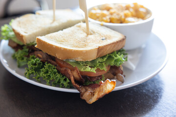 A BLT sandwich with bacon, lettuce and tomato sits on a white plate next to a bowl of macaroni and cheese
