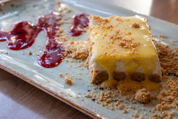 A dessert with a sauce and crumbs on served on a long plate with a raspberry sauce.