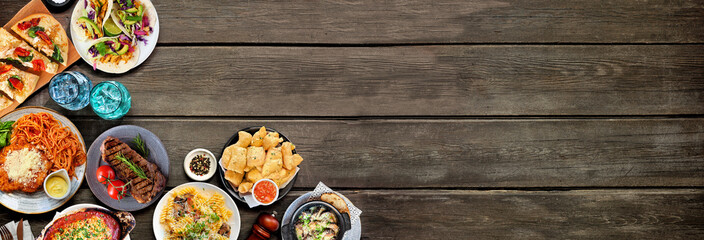 Corner border of various delicious foods. Above view on a dark wood banner background. Copy space. Pastas, flatbreads, tacos, steak and restaurant theme dishes.