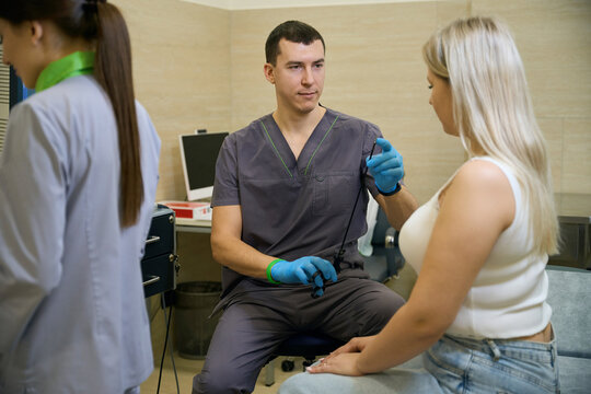 Young proctologist preparing female patient for proctoscopy