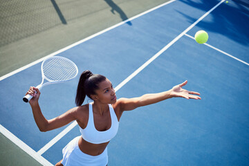 Black woman, racket and playing tennis in outdoor, confident serve and sports workout on court. Female person, fitness and ball for game or match at club, exercise and energy for training practice