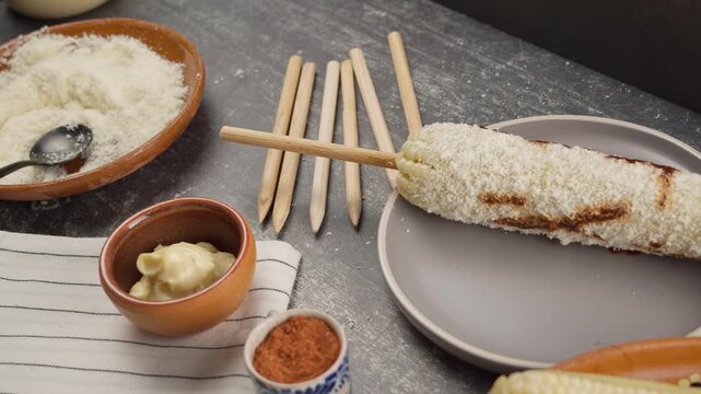 Corn prepared with the ingredients used, Mayonnaise, Aged cheese, Red sauce, Chili powder and wooden sticks