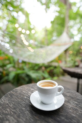 small coffee cup on weathered brown wooden table with green lush background