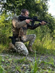 Fototapeta premium A soldier aiming a rifle. A soldier with a rifle in his hand standing in the forest. Dressed in camouflage.