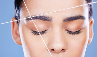 Woman, beauty and thread eyebrow in studio, cleaning and shape procedure on blue background. Female...