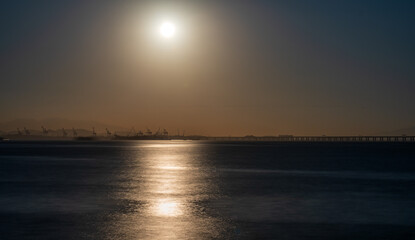 Obraz premium Tranquil Seaside Sunset with Industrial Silhouettes on Horizon