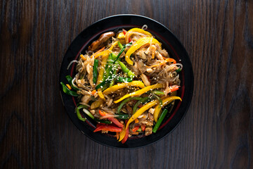 Japchae include bell pepper, capsicum, tomato, carrot, noodles and spring onion served in dish isolated on wooden table top view of korean food