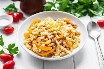 Lunch dish for the whole family: pasta with vegetables in a white plate on a white background. Close-up.