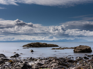 Rocky coastline stretching out to sea with mountains in the distance under cloudy sky in scotland
