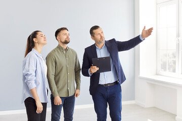 Realtor showing beautiful house to a young happy couple. Professional real estate agent shows bright new apartment. Successful family ready to become homeowners. Real estate market concept.