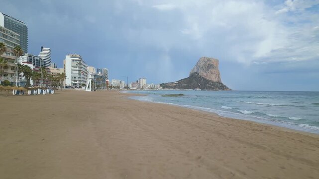 Beach with the pe&ntilde;on de ifach in the background. The sky is cloudy and the beach is empty. vertical video.