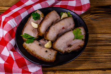 Slices of baked pork belly, garlic and parsley on a black plate