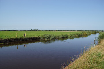 Dutch pasture landscape in North Holland. Canal called Bergervaart through the meadows to the village of Bergen. Netherlands. Blue sky. Summer, July