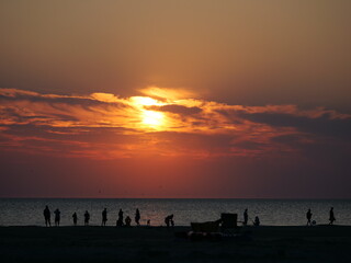 Red-orange sunset on the beach, in the foreground people whose black outlines are recognizable