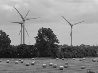 foreground hay bales on a field, in the background wind turbines, black and white photos