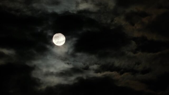 Full moon in the night sky with flying black clouds. Cloudy dark sky and moonlight in spooky feeling like thriller and horror films. Real video recording