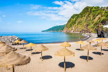 Sun umbrellas on beach in Povoacao town and green hills in background, Sao Miguel island, Azores,...